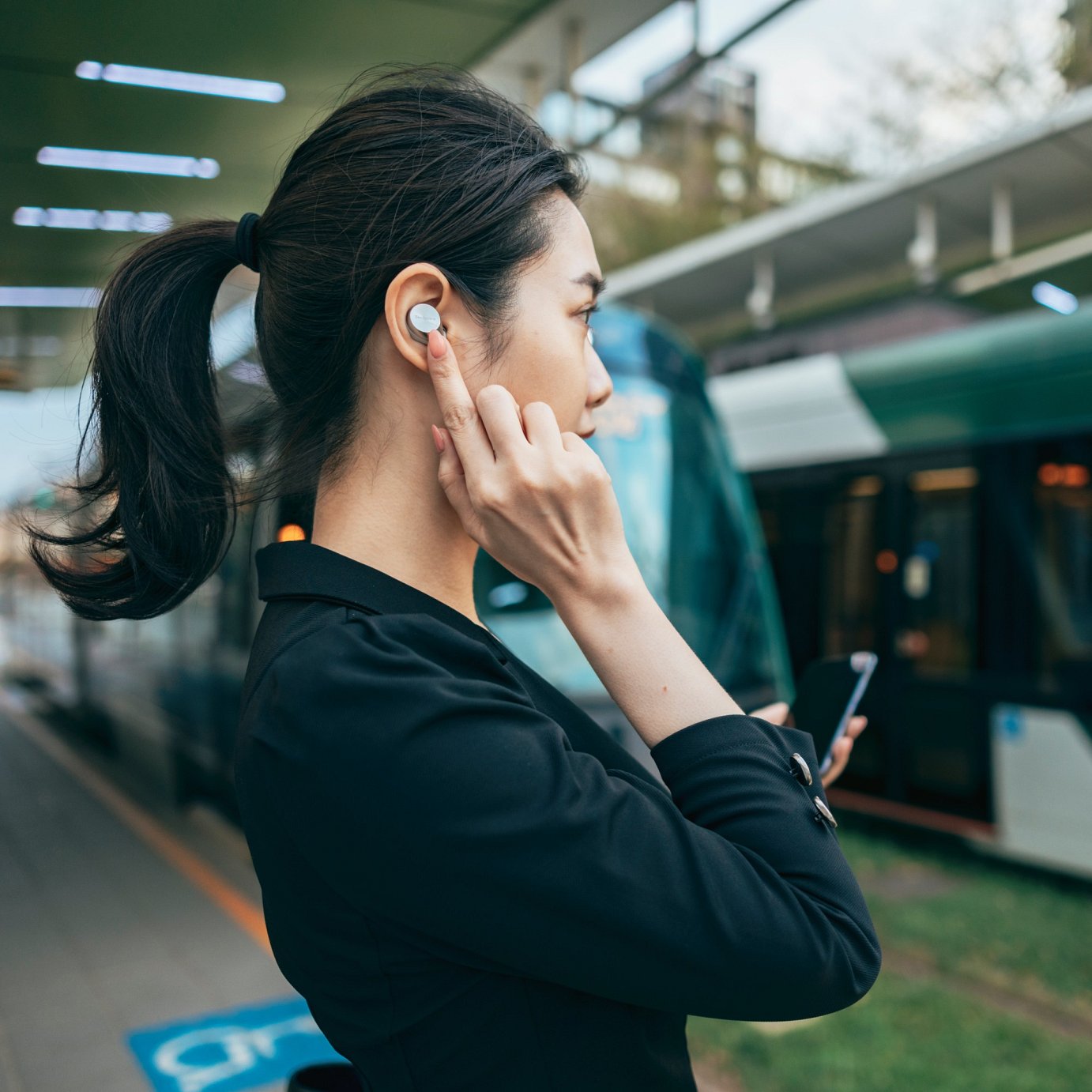 An Asian female businesswoman uses a Bluetooth headset and mobile device to work remotely and discuss work projects with colleagues outside the office while waiting for the subway. By connecting the Bluetooth headset to the mobile device, she can also listen to music or work remotely, communicating and interacting with clients or subordinates during her commute.